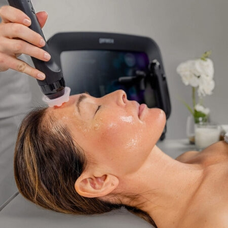 Esthetician using a Glo2 facial device on a woman's forehead during a professional treatment