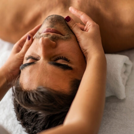 Esthetician performing a relaxing facial massage on a male client lying on a spa table