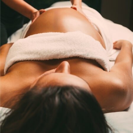 Pregnant woman receiving a gentle prenatal massage while lying on her back with expert towel draping at Natural Body.