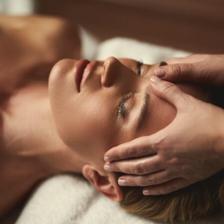 Woman receiving a calming face and shoulder massage while lying on a spa table.