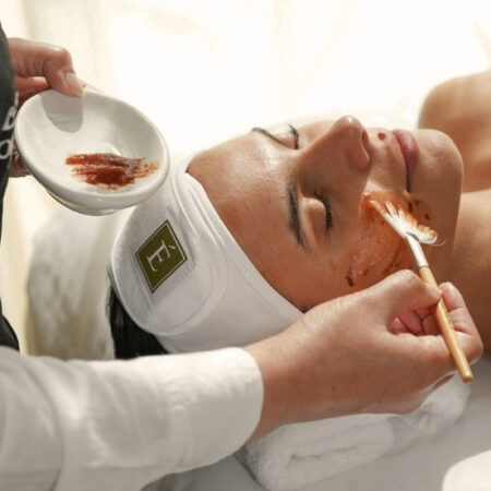 Esthetician applying a natural facial mask with a brush to a woman’s face using Eminence products