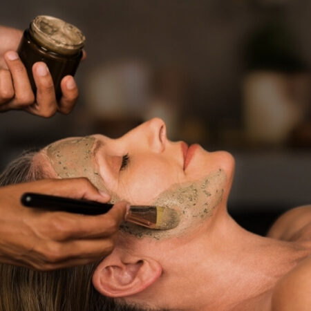 Close-up of a clay-based facial mask being applied to a woman's face with a brush