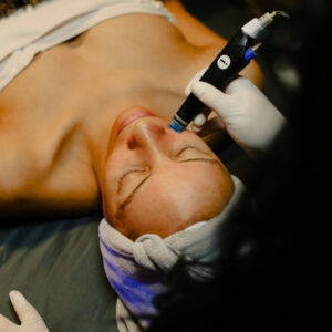 Spa guest lying down with eyes closed while esthetician performs Hydrafacial with handheld tool