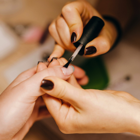Applying dark brown nail polish during a spa manicure session at Natural Body Spa + Med Spa.