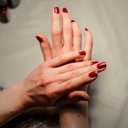 Woman's hands resting gently together, showcasing a fresh manicure with glossy red nail polish at Natural Body Spa.