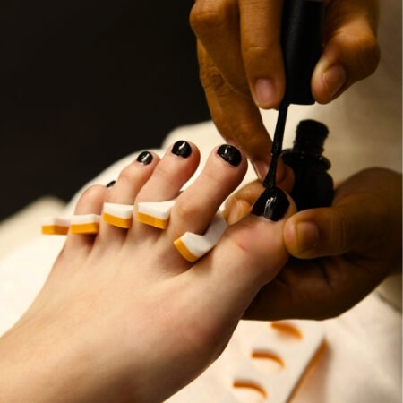 Spa technician painting toenails with dark polish as part of a relaxing pedicure at Natural Body Spa.