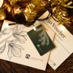 Natural Body Spa holiday gift card and $50 holiday voucher displayed on table with gold holiday tree